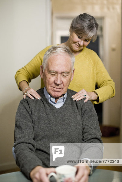 Seniorin gibt dem Mann zu Hause eine Schultermassage