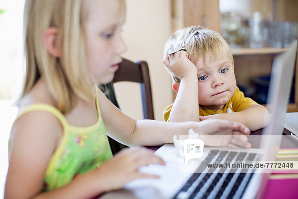 Little boy sitting with sister using laptop at table