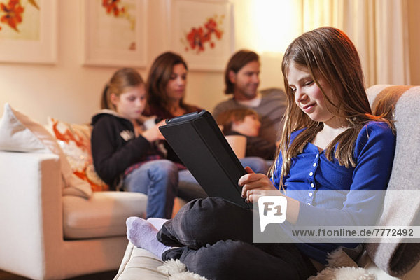 Girl using digital tablet with family sitting on sofa in living room