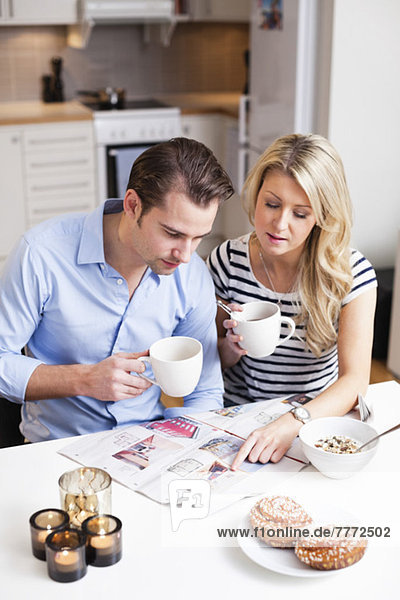 Couple reading property advertisements in newspaper while having coffee at breakfast table