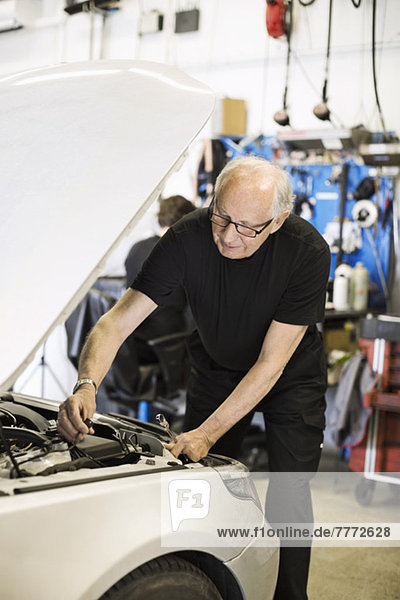 Senior male mechanic working on car engine at auto repair shop with coworker