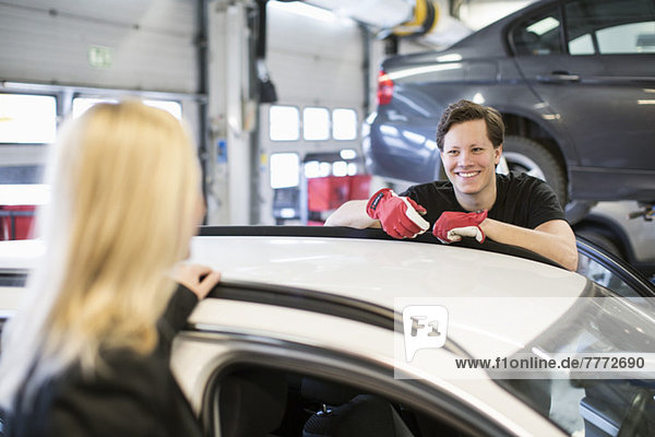 Happy mechanic looking at female customer over car at workshop