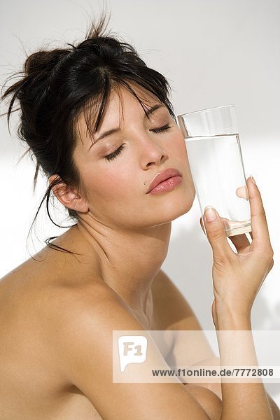 Young woman holding glass of water against her cheek