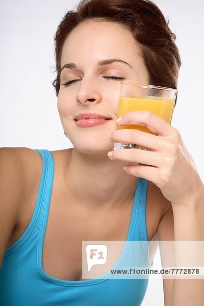 Porträt einer jungen brünetten Frau mit geschlossenen Augen und einem Glas Fruchtsaft an der linken Wange.