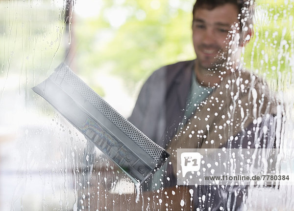 Mann wäscht Fenster mit Rakel