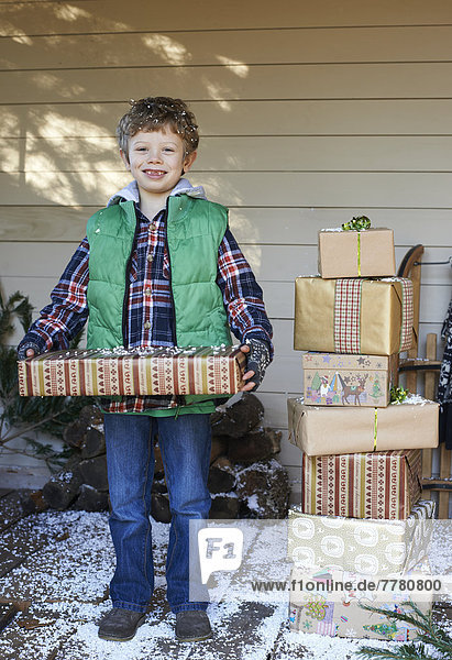 Junge mit Weihnachtsgeschenken auf verschneiter Veranda