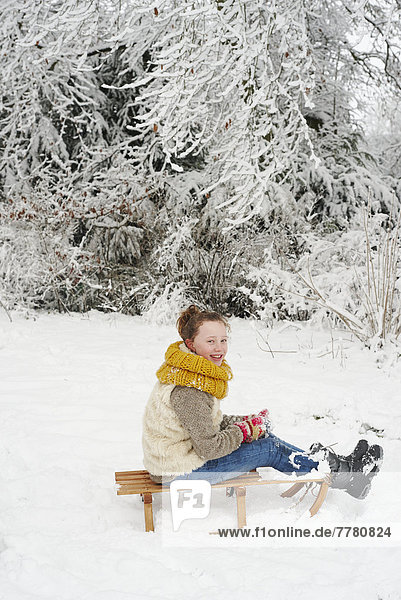 Mädchen auf Holzschlitten im Schnee sitzend