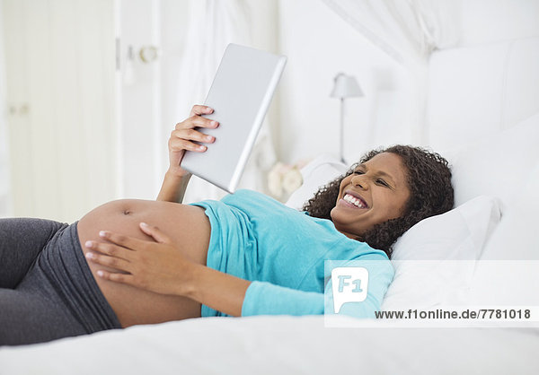 Schwangere Frau mit Tablet-Computer im Bett