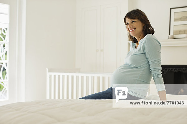 Schwangere Frau sitzt auf dem Bett