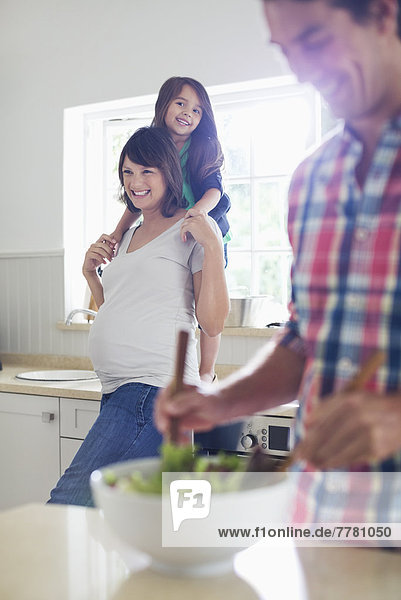 Schwangere Mutter und Tochter sehen Vater beim Salatwerfen zu.