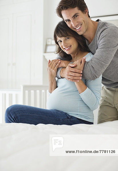 Mann umarmt schwangere Freundin im Bett