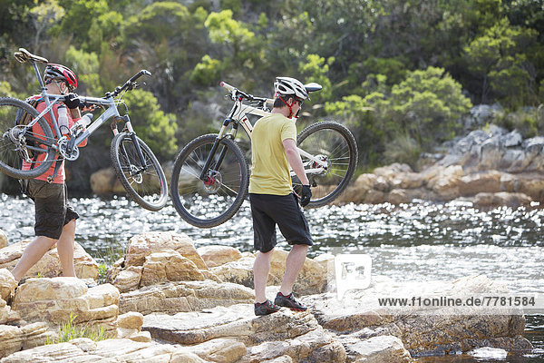 Men carrying mountain bikes on rock formation