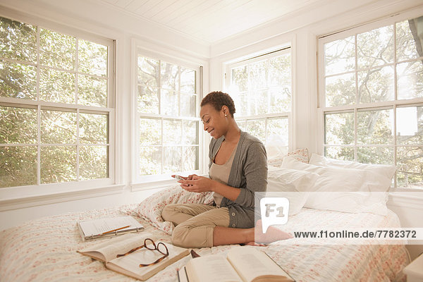 African American woman studying in bed and using cell phone