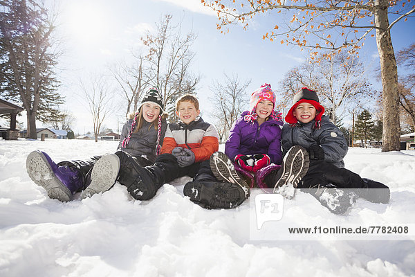 Caucasian children sitting in snow outdoors