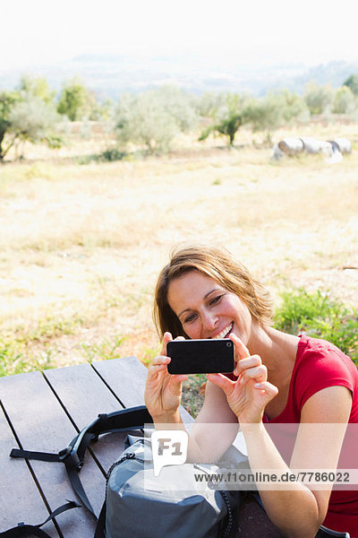 Woman sitting at picnic bench photographing self with camera phone