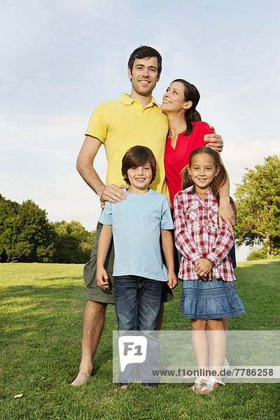 Porträt einer Familie mit zwei Kindern auf Rasen stehend