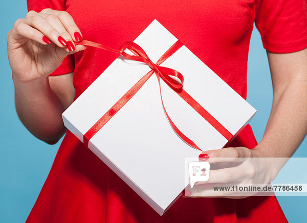 Frau öffnet weiße Geschenkbox mit roter Schleife,  Mittelteil