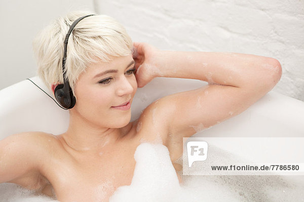 Woman in bubble bath wearing earphones