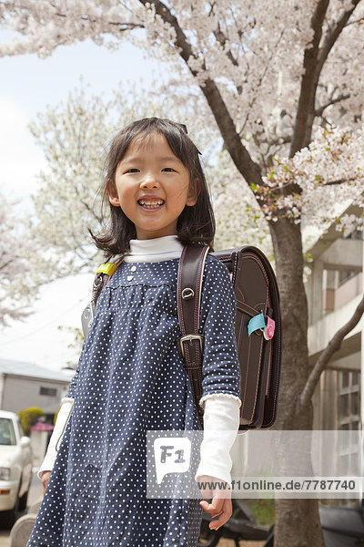 Young child with schoolbag under a cherry tree.
