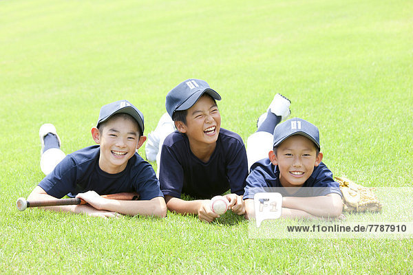 Boys in baseball uniforms lying on grass