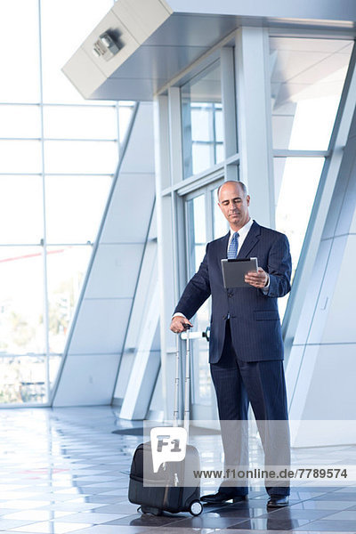 Mature businessman with digital tablet and suitcase