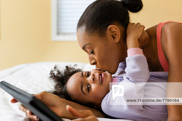 Mother kissing daughter and holding digital tablet