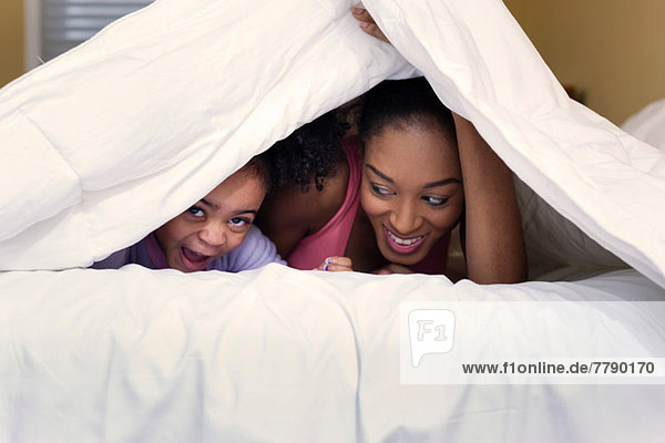 Mutter und Tochter spielen auf dem Bett und verstecken sich unter der Bettdecke.