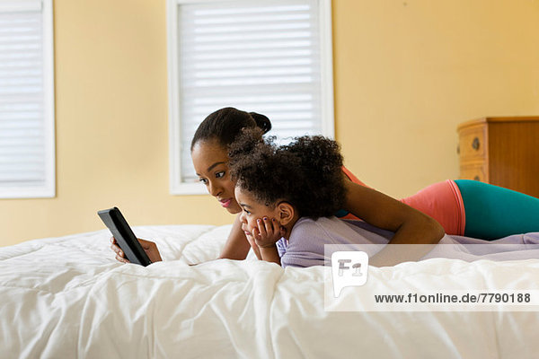 Mother and daughter lying on bed using digital tablet