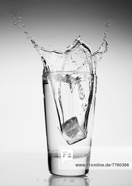 Eiswürfel  der in ein Glas Wasser fällt.