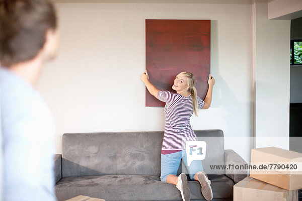 Young couple moving house  woman hanging painting