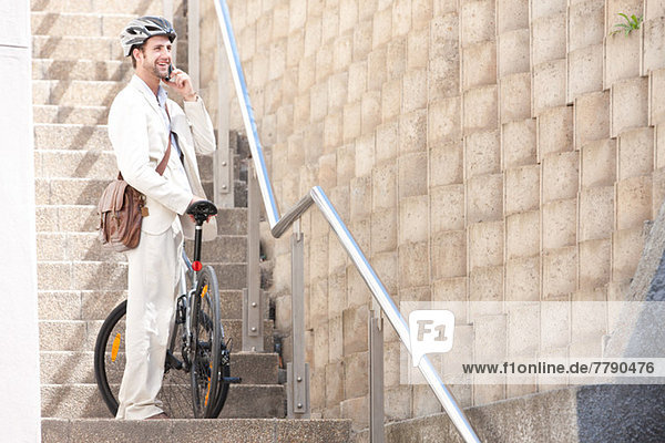 Junger Mann auf Stufen auf dem Handy mit Fahrrad