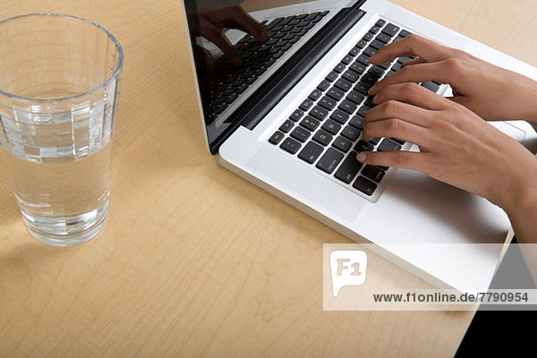 Woman using laptop with glass of water