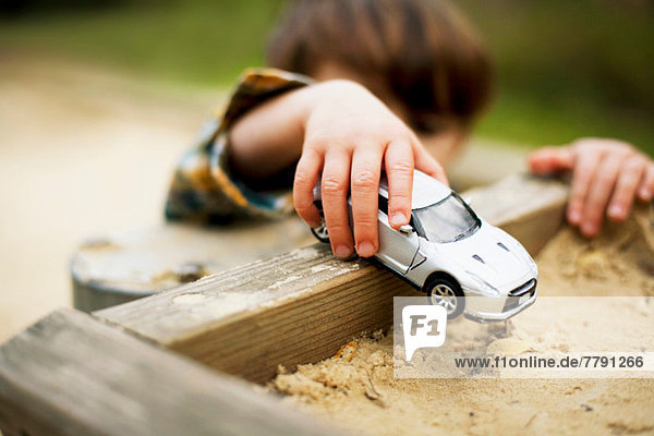 Male toddler holding toy car above sandpit