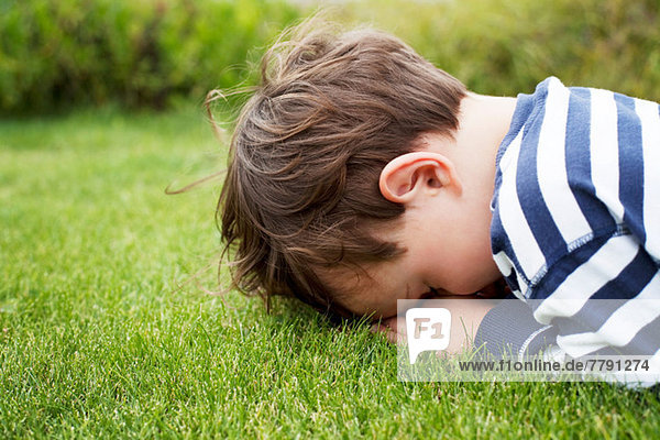 Männliches Kleinkind versteckt sich mit dem Gesicht nach unten auf Gras.