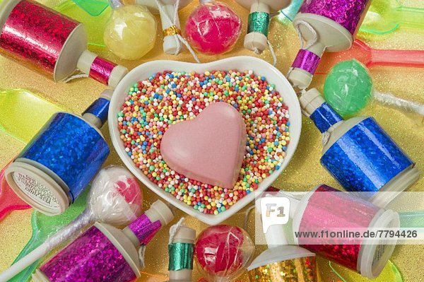 Herzschale mit einem rosa Schokoladenherz  bunte Party Poppers  Lollis und Kunststoffeislöffel