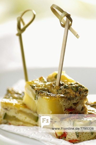 Mehrere Portionen Kartoffeltortilla mit Zucchini  Knoblauch  Chili und Minze auf Spiesschen