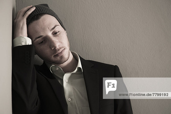 Portrait of Young Man wearing Woolen Hat and Suit Jacket  Looking Downward  Absorbed in Thought  Studio Shot