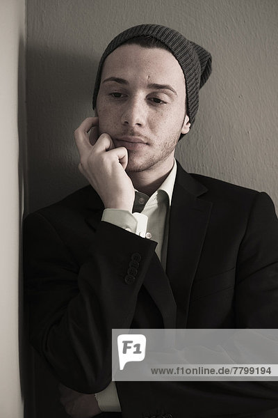 Portrait of Young Man wearing Woolen Hat and Suit Jacket  Looking Downward  Absorbed in Thought  Studio Shot
