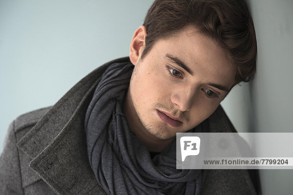 Head and Shoulder Portrait of Young Man wearing Grey Scarf and Jacket  Absorbed in Thought  Studio Shot on Grey Background