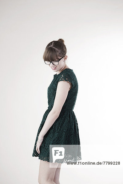 Portrait of Young Woman wearing Green  Lace Dress and Horn-rimmed Eyeglasses  Looking Downward and Smiling  Studio Shot on White Background