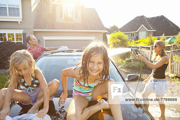 A family washes their car in the driveway of their home on a sunny summer afternoon in Portland  Oregon  USA