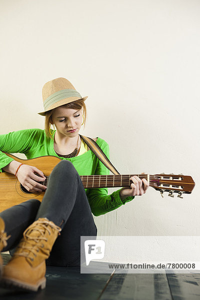sitzend  Portrait  Jugendlicher  Boden  Fußboden  Fußböden  Spiel  Hut  Gitarre  Akustikgitarre  akustische Gitarre  Kleidung  Mädchen