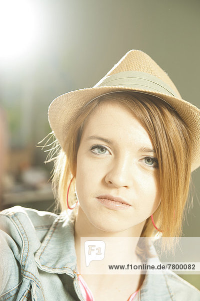 Head and shoulders portrait of teenage girl wearing hat in studio.