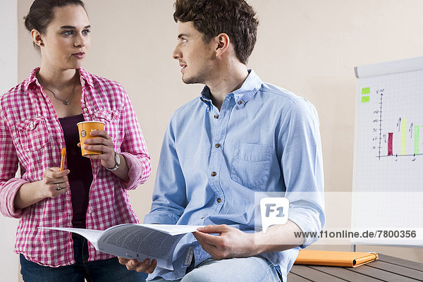 Young Businessman and Young Businesswoman Discussing Document in Office