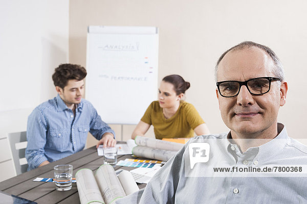 Portrait of Mature Businessman wearing Eyeglasses with Colleagues Meeting in the Background