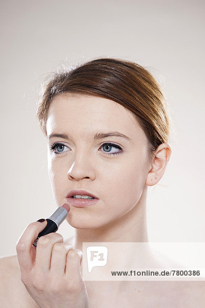 Portrait of Teenage Girl Applying Lipstick in Studio Shot on White Background