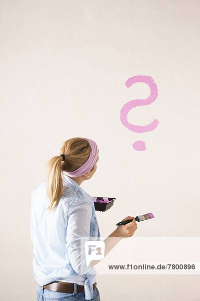 Studio Shot of Young Woman Painting a Question Mark on a Wall