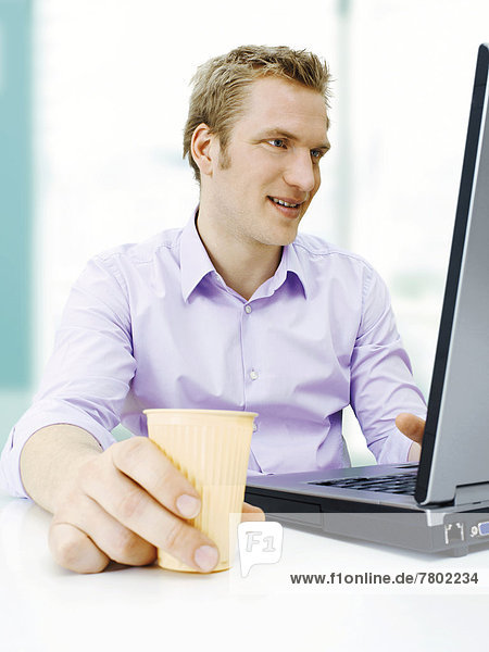 Businessman working on a laptop  holding a plastic cup