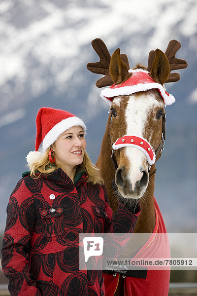 Junge Frau mit Weihnachtskappe und Pferd mit weihnachtlichem Rentiergeweih