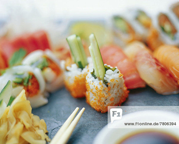Verschiedene Sushirollen mit eingelegtem Ingwer und Stäbchen auf Schieferplatte